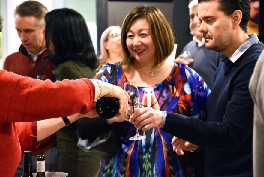 People mingling while wine is poured into their glasses. 