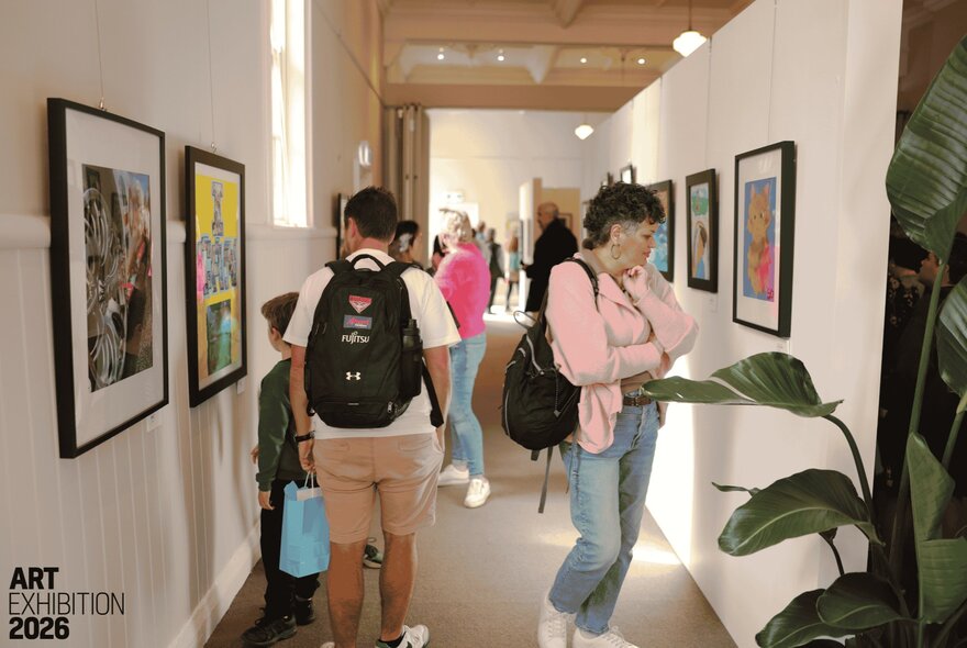 People in a corridor viewing artwork the walls. 