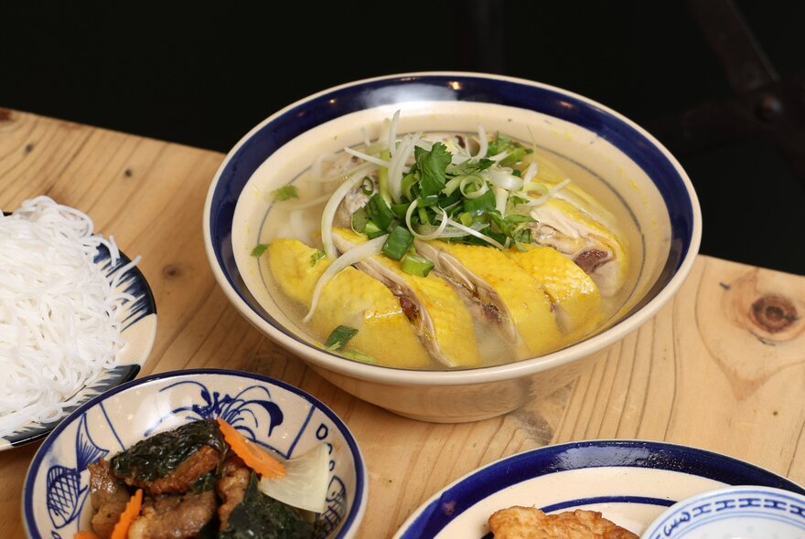 A Vietnamese soup in a round bowl with smaller dishes of ingredients alongside it.