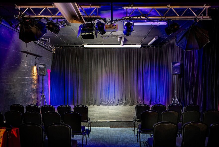 The small empty stage at Club Voltaire, with rows of theatre chairs in front of it.