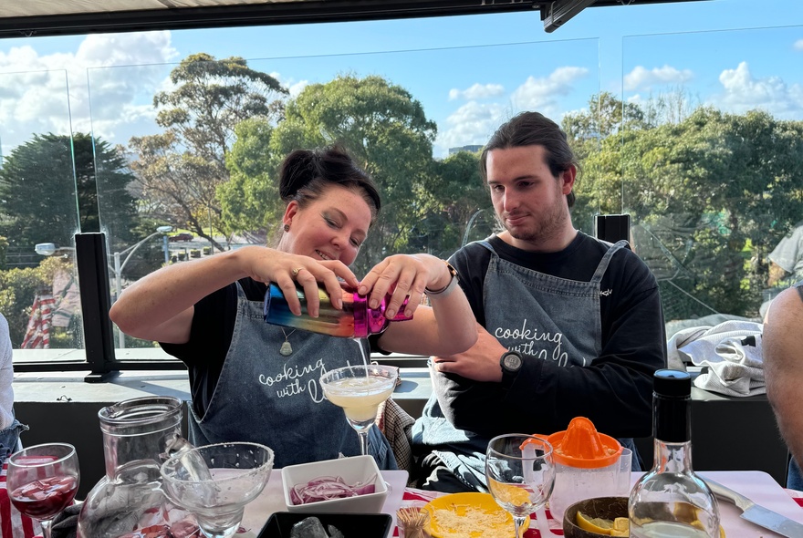 Participants at a cooking class learning how to make cocktails, a large window behind them.