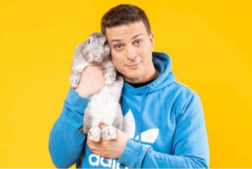 Man wearing a blue hoodie holding a large white rabbit.