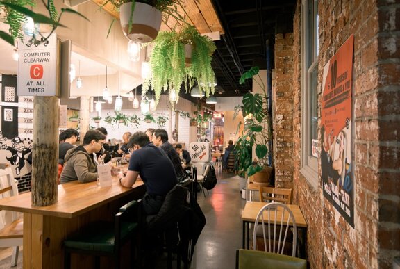 People seated at a venue table with plants and signs.