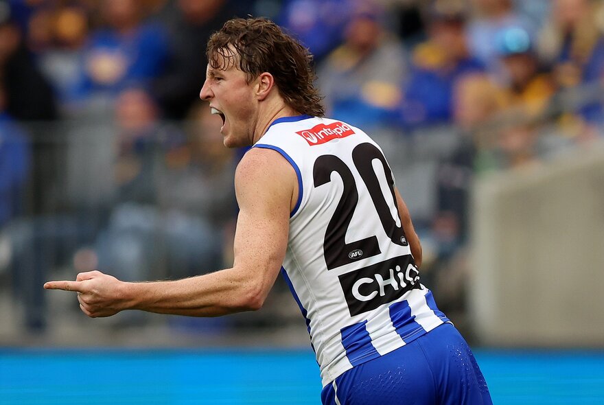A North Melbourne AFL player cheering himself on the field with his mouth open and his finger pointing at something.