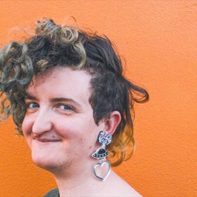 A smiling woman with short curly hair and a long, chunky earring.