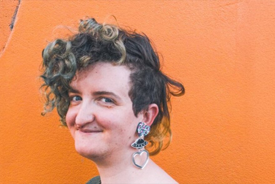 A smiling woman with short curly hair and a long, chunky earring.