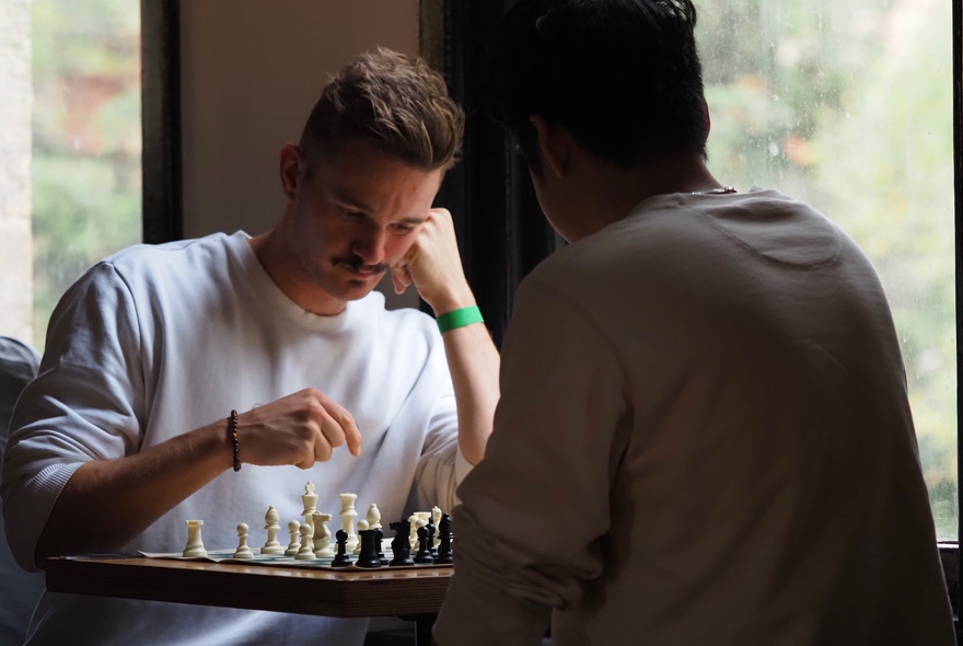 A social chess gathering with two people playing chess in an indoor setting.