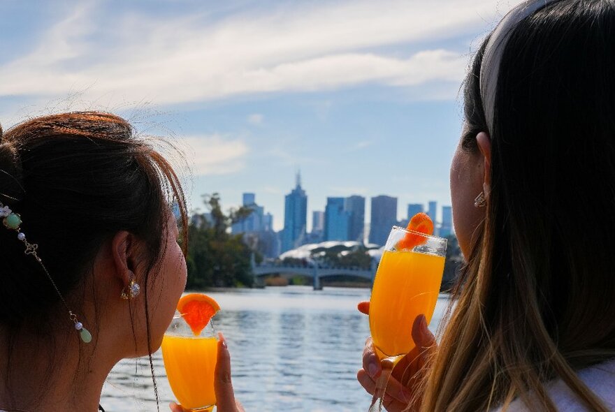 The back of two women sipping mimosas while looking at the city from the river. 