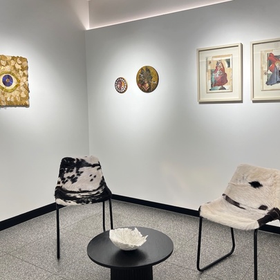 A gallery setting with artwork on the walls, and two chairs and a black coffee table.