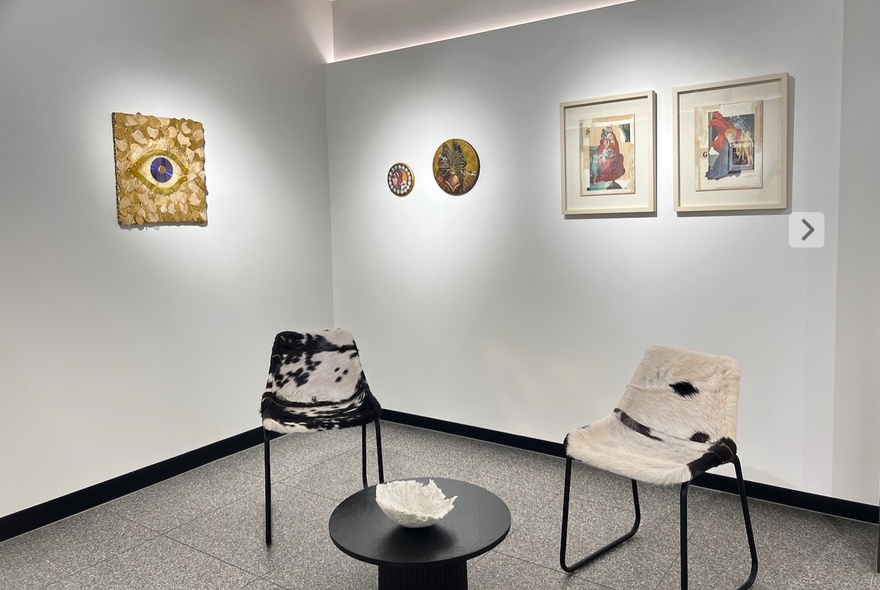 A gallery setting with artwork on the walls, and two chairs and a black coffee table.