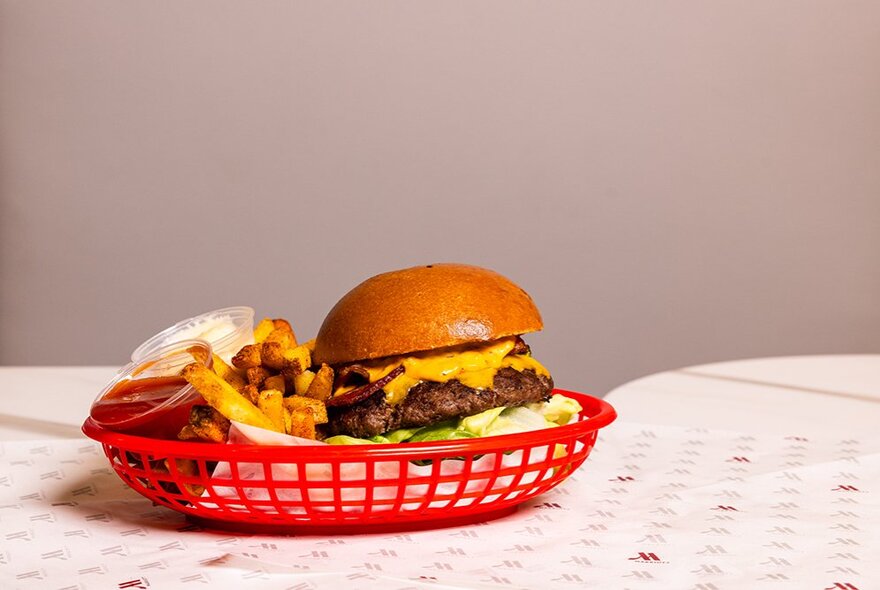 A classic cheeseburger with lettuce and cheese, plus fries in a red basket, on a restaurant table.