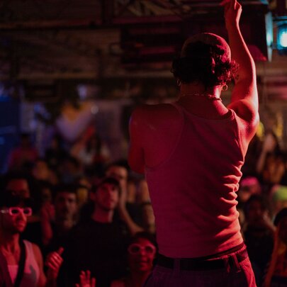A performer on a stage, seen from behind with an audience in front of him.