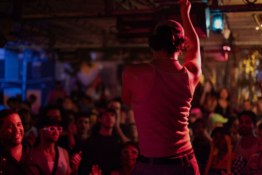 A performer on a stage, seen from behind with an audience in front of him.