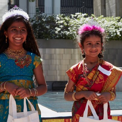 Two young girls dressed in traditional Indian attire and accessories during a cultural or Diwali celebration in an open air space.