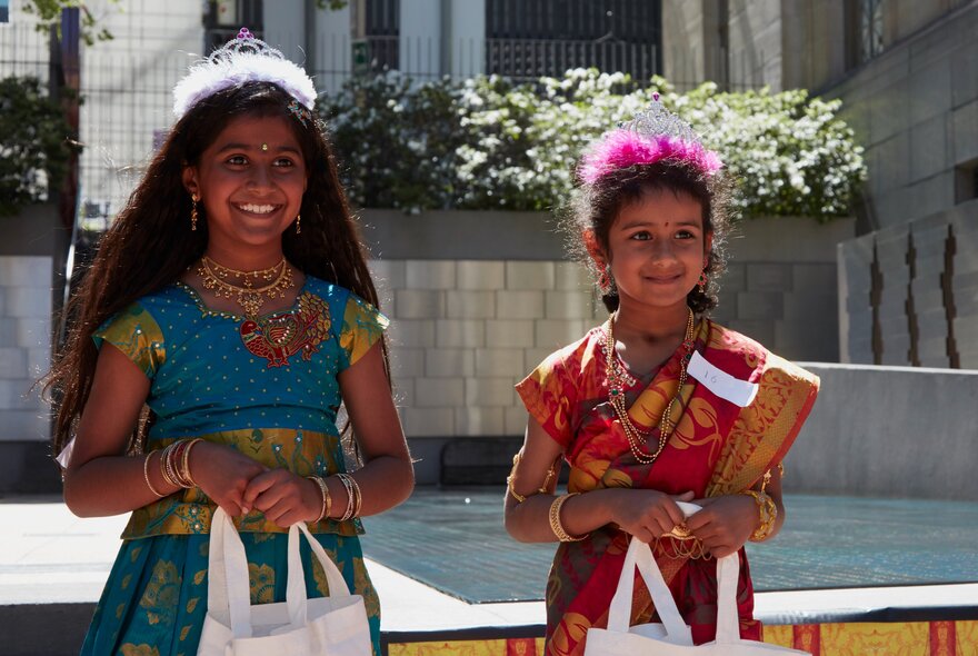 Two young girls dressed in traditional Indian attire and accessories during a cultural or Diwali celebration in an open air space.