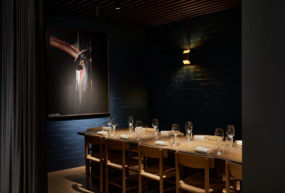 A dark dining room with modern art and a long table.