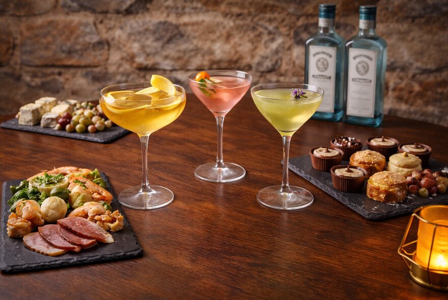 Three coloured gin-based cocktails with platters of snacks.