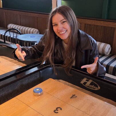 Smiling woman seated at a table in a venue, pointing at a buzzer.