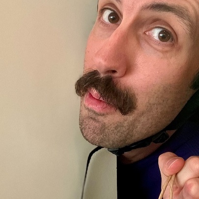 A man with a moustache peeking around a door with a helmet strap under his chin. 