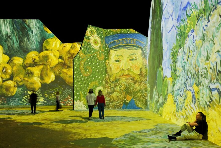 People walking around a very large exhibition space with Vincent van Gogh's paintings digitally projected on all the wall and floor spaces.