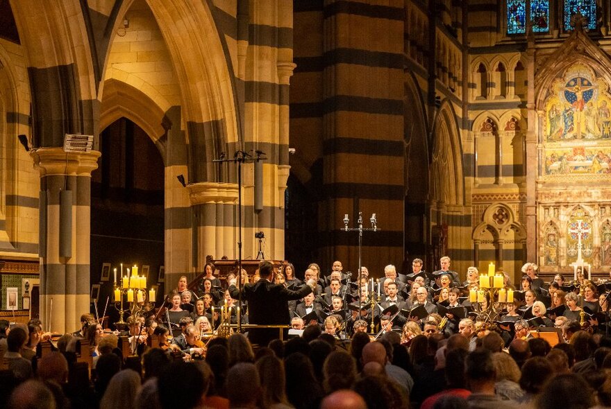 The interior of St Paul's Cathedral, with a choir and orchestra performing, and an audience seated in the pews listening.