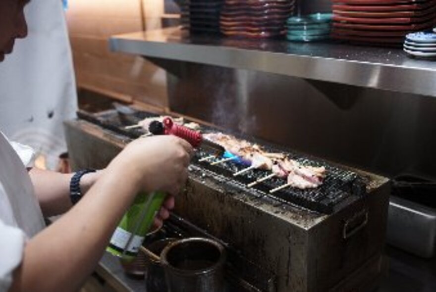 A cook grilling yakitori skewers in a commercial kitchen.