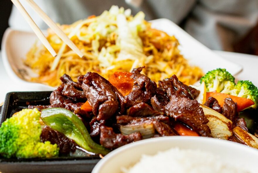 Sizzling beef on a hot plate, with a plate of noodles in the background.