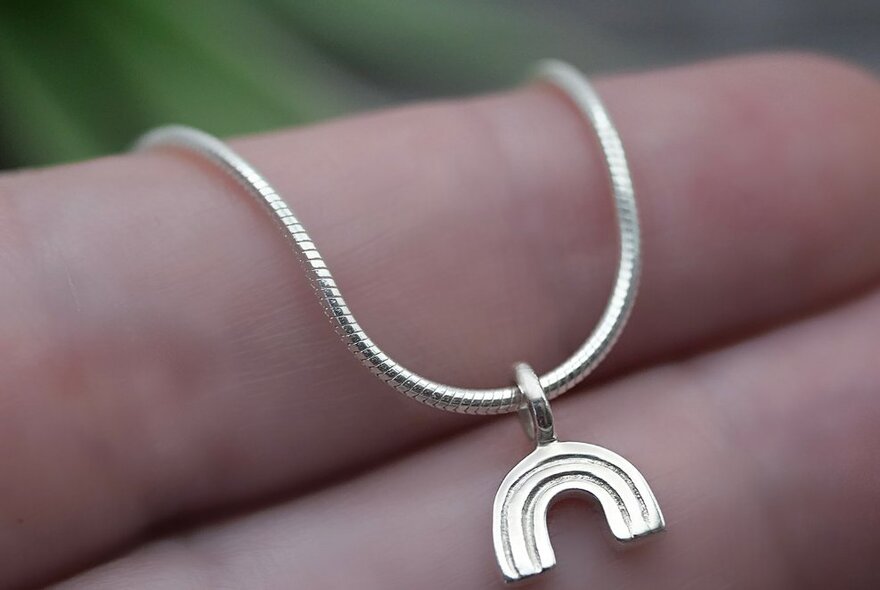 A hand holding a silver necklace that has an arch shaped pendant hanging from it.