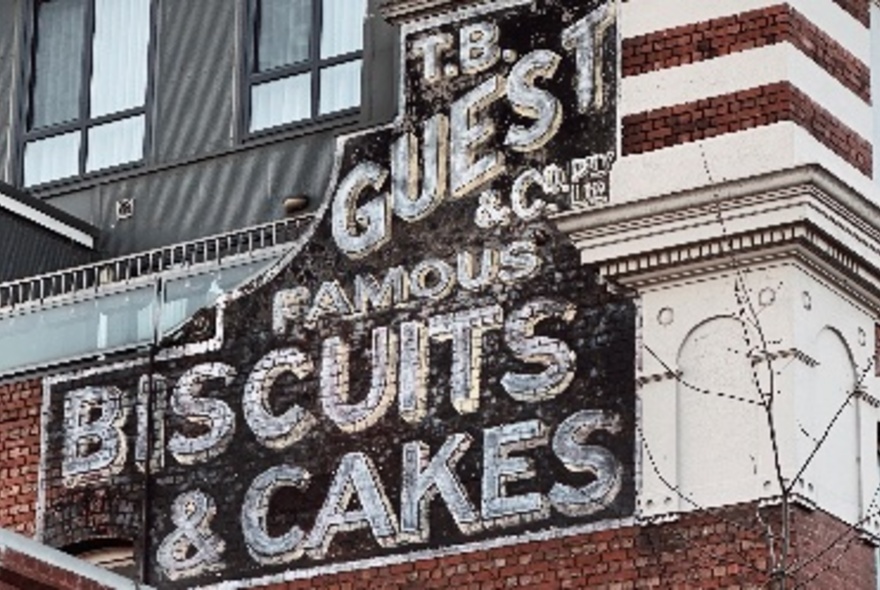 An old biscuits and cakes sign on a the side of a building. 