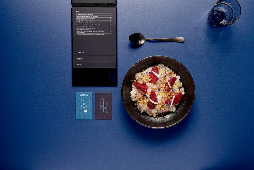 Bowl of tapioca and fruit on a blue table with an open menu next to it.