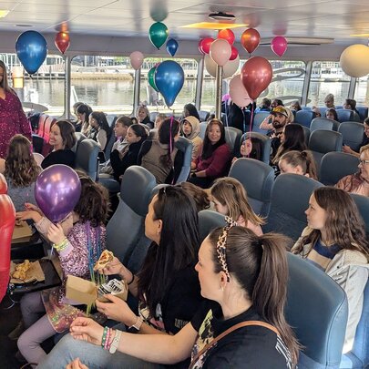 A crowd of people celebrating inside a decorated ferry during a Taylor Swift-themed singalong cruise. 