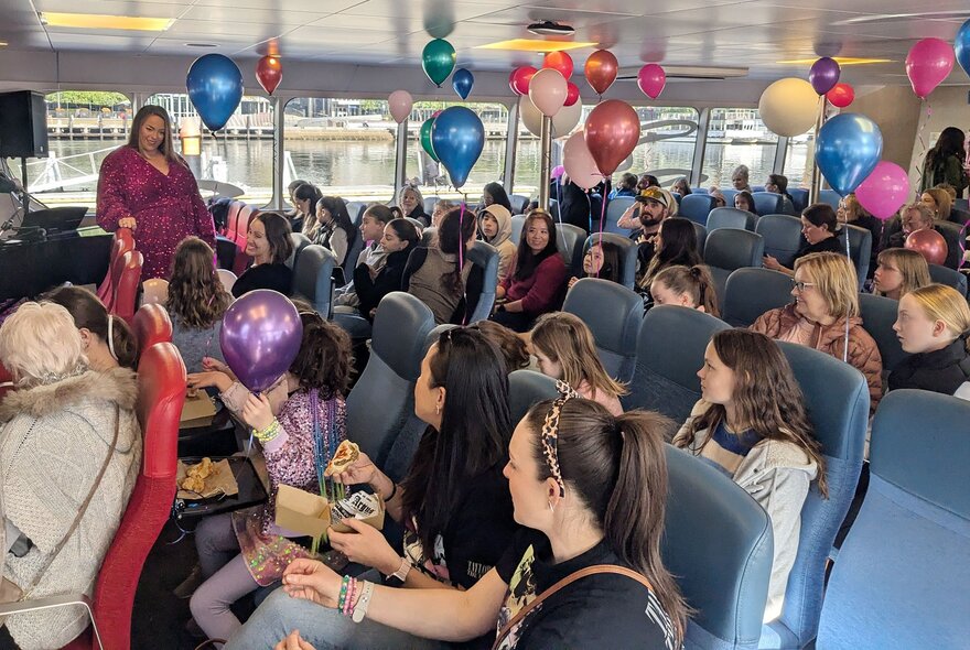 A crowd of people celebrating inside a decorated ferry during a Taylor Swift-themed singalong cruise. 