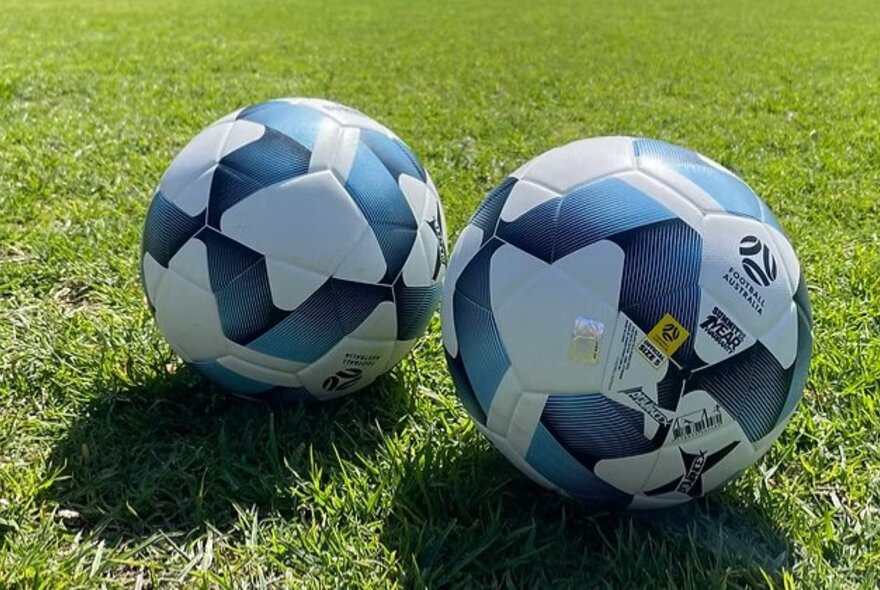 Two soccer balls on a grass pitch.