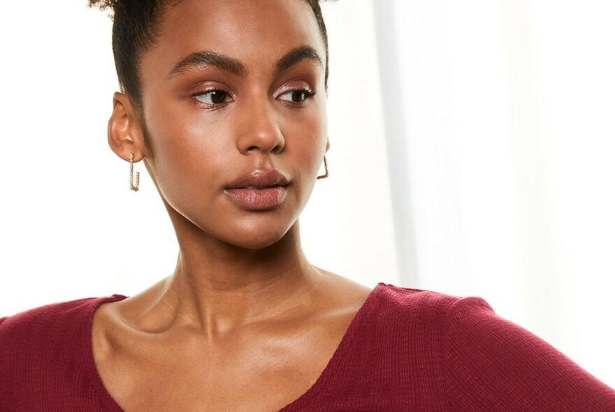 Model with dark hair pulled back, silver square earrings and red scoop neck top.