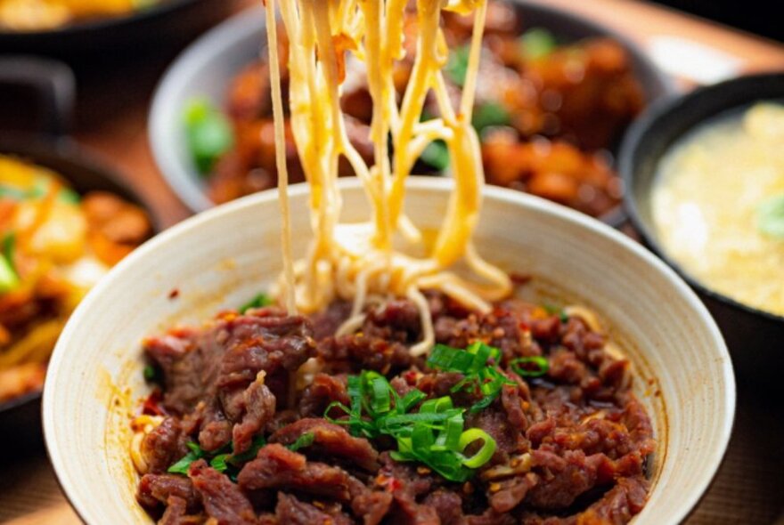 Bowl of meat and noodles, with noodles being added to the bowl.