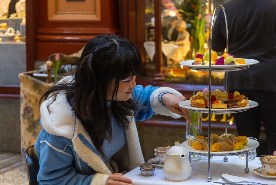 A woman is choosing a cake from a cake stand.