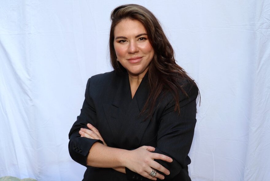 A woman wearing a black blazer with arms crossed, in front of a white background.