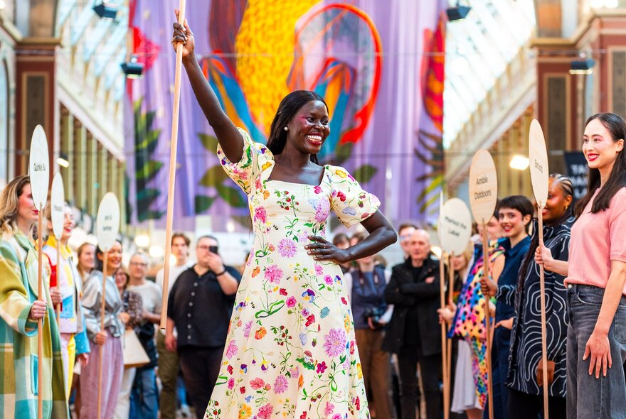 Woman holding a stick, wearing a floral dress while onlookers look on.
