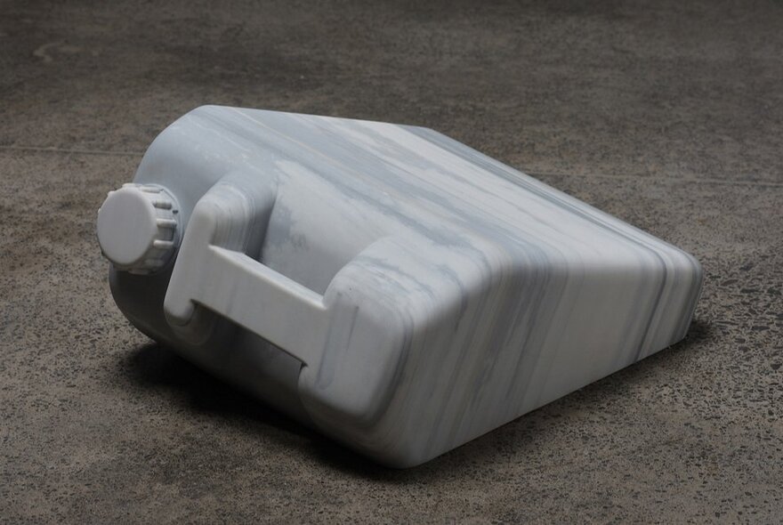 A carved marble sculpture shaped like a plastic jerrycan sitting on a grey surface.