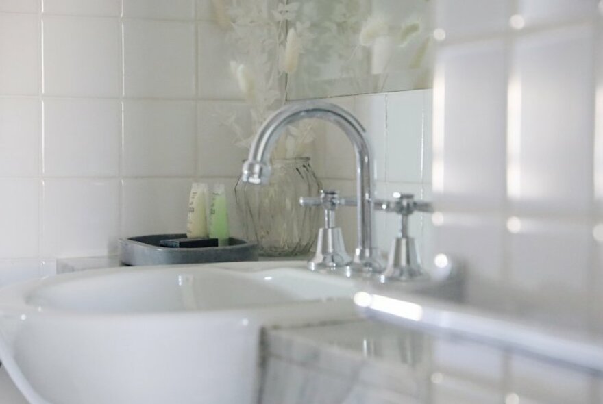 A basin and tapware in a glossy white bathroom with small shampoo and conditioner bottles in the background.