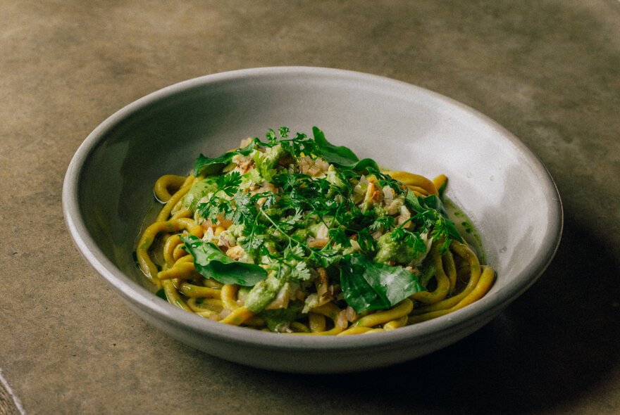A bowl of parsley-topped pasta on a concrete background.