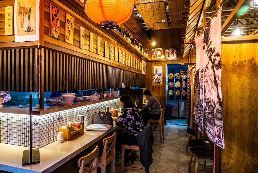 People dining at the counter of a Japanese restaurant.