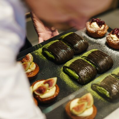 Out of focus person in white leaning over a selection of pastries. 