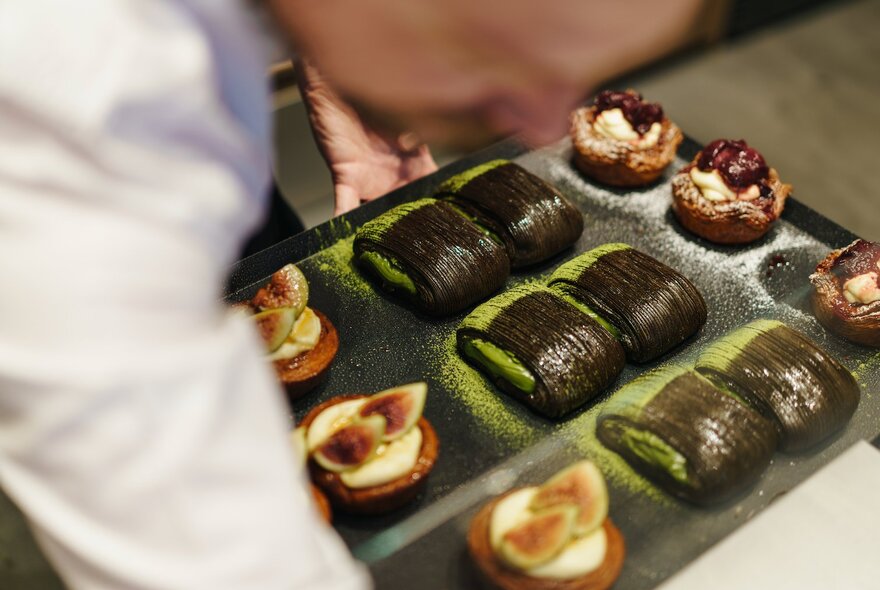 Out of focus person in white leaning over a selection of pastries. 