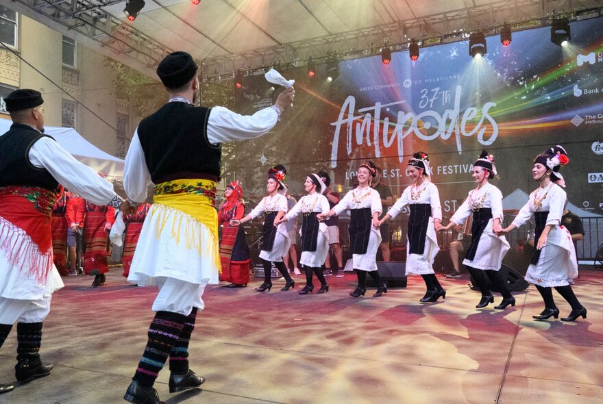 Greek dancers performing on a stage wearing skirts and boots.