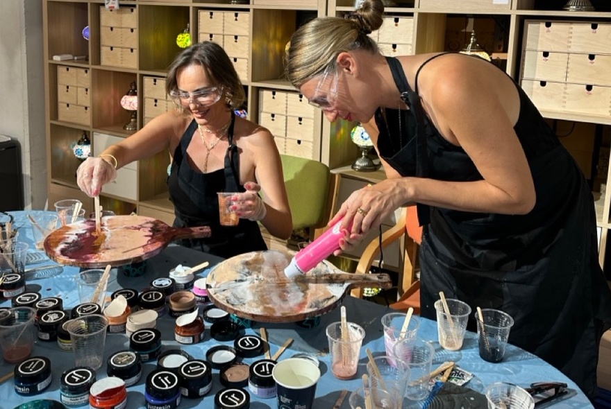 People working at a crafts table in a studio with pots of resin and cheese boards.