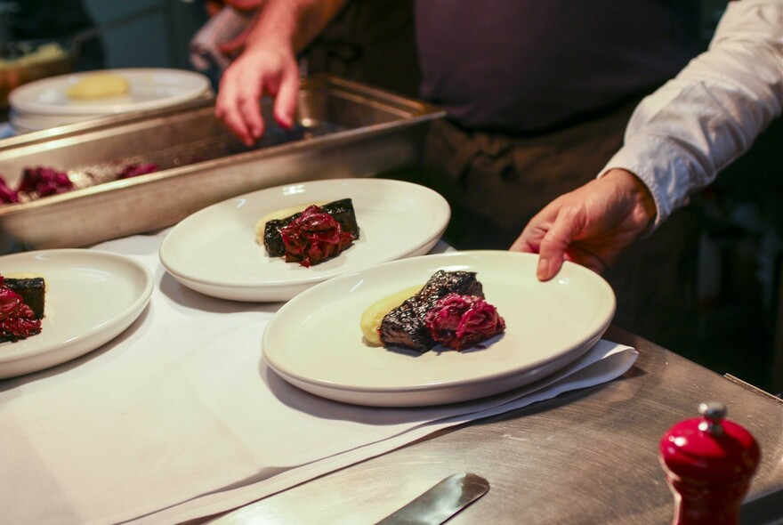 Waiter taking a plate of steak from a food serving area.