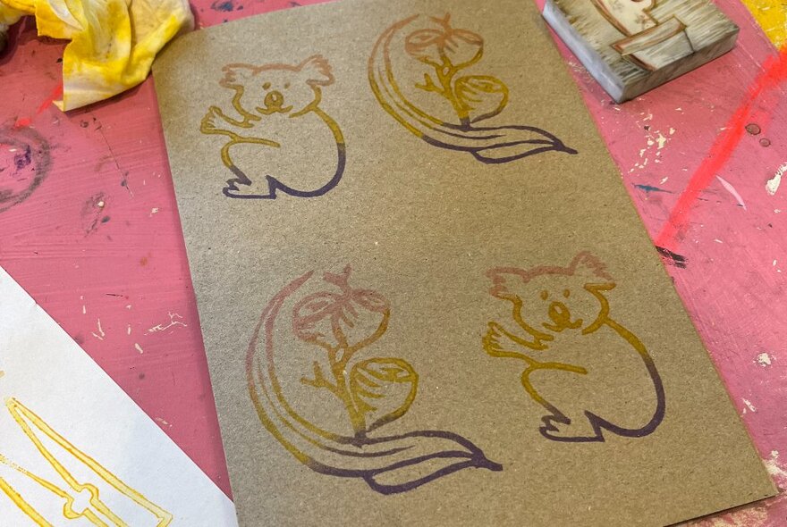 Images of koalas and gumnuts on a brown piece of cardboard, at a craft table.