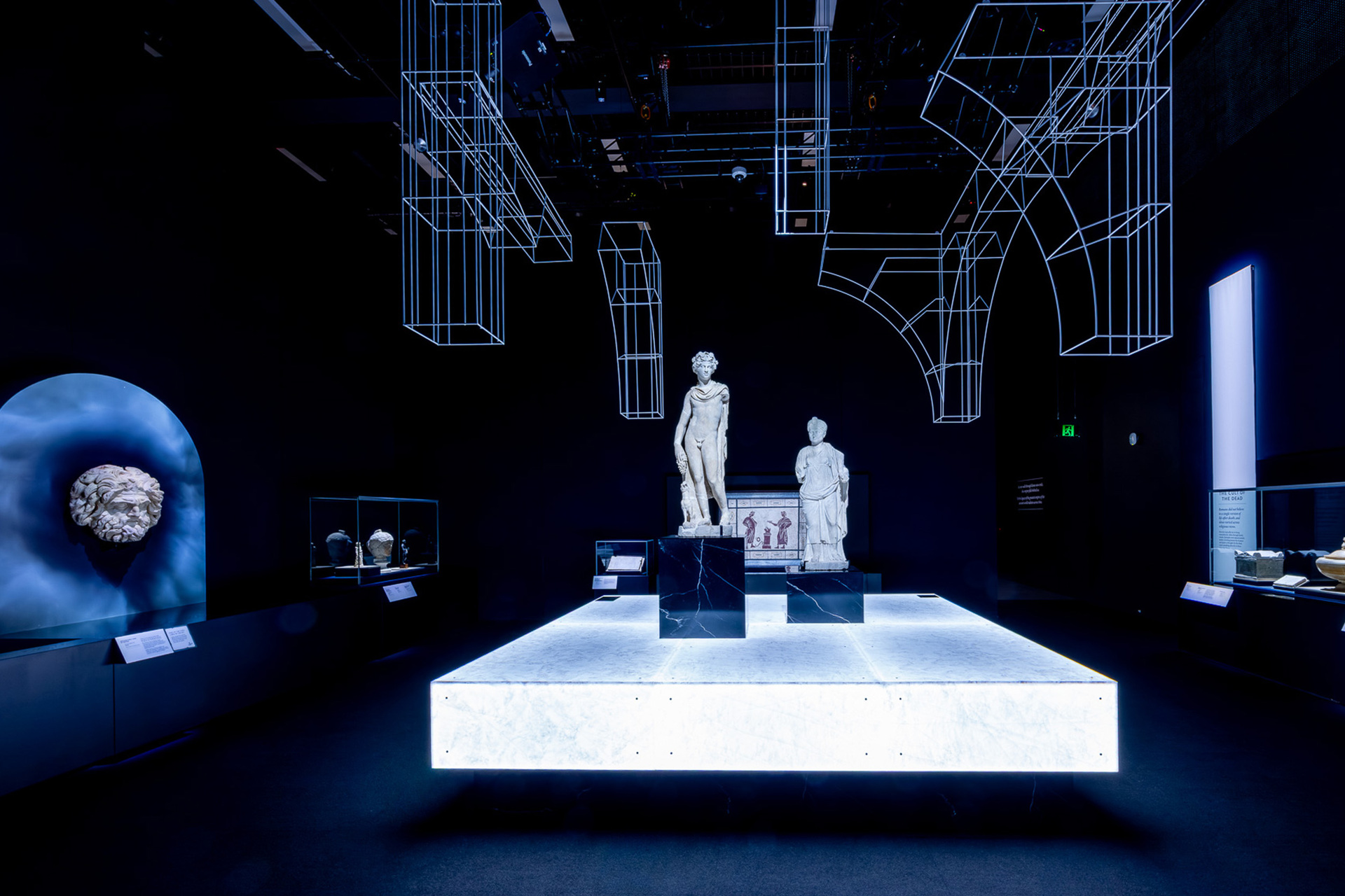 A gallery space with Roman statues, neon lights and Roman busts in it