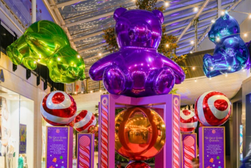 Three large, colourful and shiny gummy bears as part of a Christmas installation inside a shopping mall.